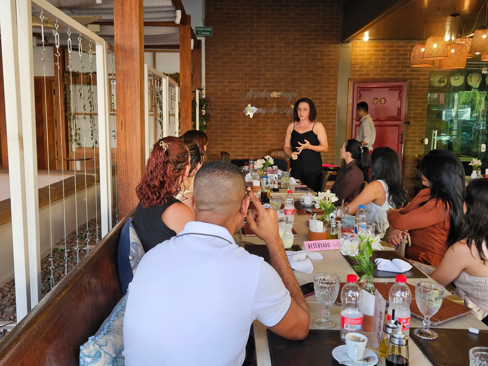 Mulher de preto em pé conversando com participantes ao redor da mesa